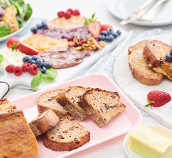 Brunch spread of Artisan bread, sliced with butter, fruit and dinner wear on pastel plates