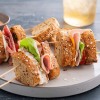 Multi-grain artisan bread sandwich pieces on skewers laying on a white plate with a slate background