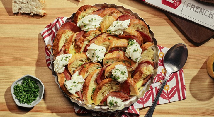 Dish of eggs Benedict casserole cooked inside a metal tin on a butcher block counter