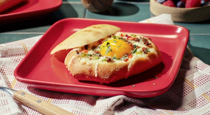 Breakfast bowl made of French dinner roll with sausage and eggs on red square plate