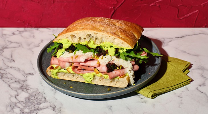 artisan bread Mortadella sandwich on gray plate with green napkin on a marble counter with red stucco wall