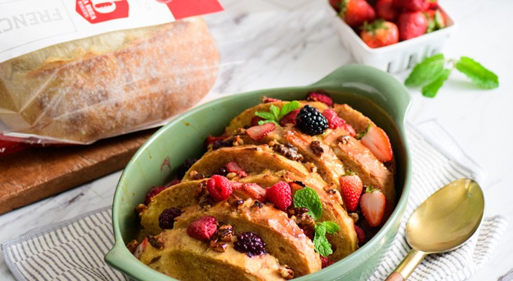 A baked overnight French toast casserole served in a sage green ceramic dish.