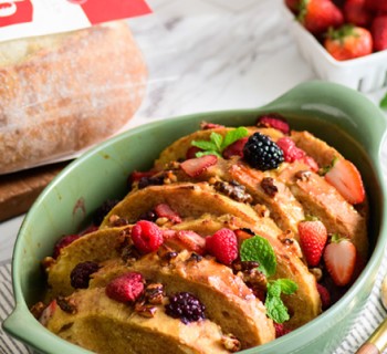 A baked overnight French toast casserole served in a sage green ceramic dish.